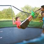 Cooper, Ashton, and Dennis Jr. (in the air) play on a trampoline 