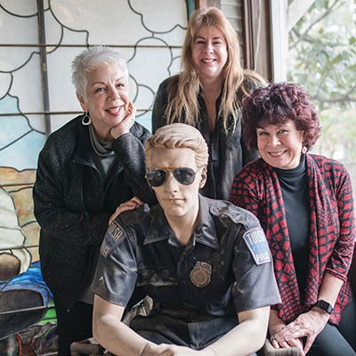 From left: Artists Melanie Fry, Cynthia Marcoux, and Kim Doner pose for a photo with the mannequin on Marcoux’ front porch.