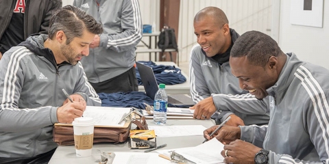 Coach Larry Nsien (second from right) flashes a smile as he works on paperwork with Roughnecks staff.