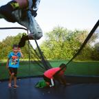 Cooper, Ashton, and Dennis Jr. (in the air) play on a trampoline 